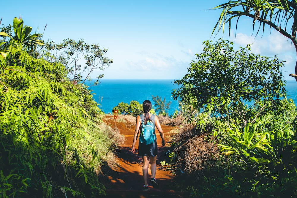 woman hiking a trail on Kauai overlooking the ocean
