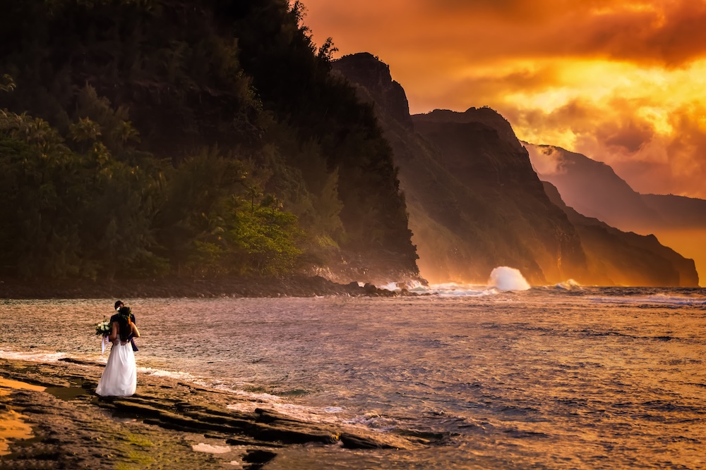 newly married couple standing on beach looking at ocean in Kauai at sunset