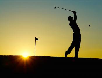 silhouette of a golfer pitching the ball toward the green at a poipu golf course at sunrise.