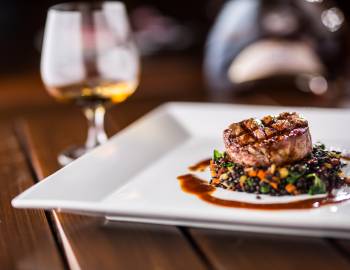 beautifully plated steak with beverage in background