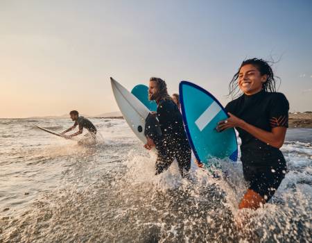 three people running into the surf with their boards
