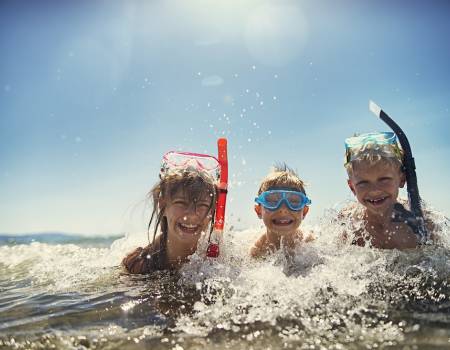 Three kids lying in the surf wearing snorkel gear on their heads