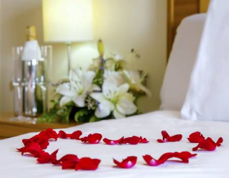 Red rose petals arranged in a heart on a white bed in a Kauai vacation rental