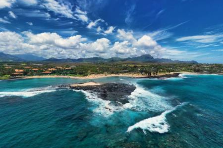 an aerial view of a clear day at poipu beach, shot over the ocean