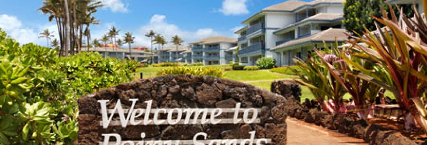 a stone sign with "Welcone to Poipu Sands" in white font