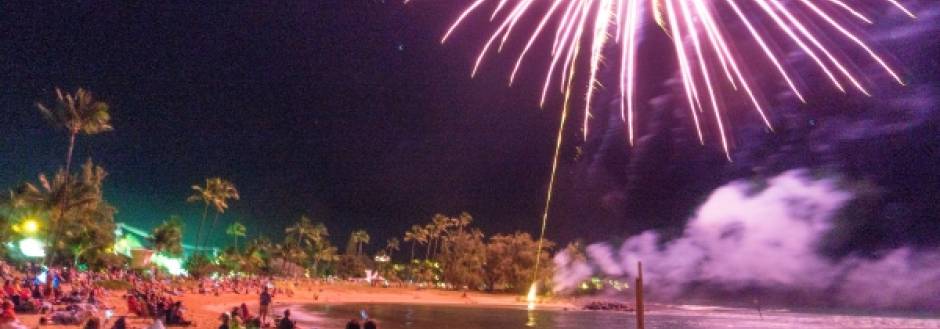 A crowd sits along Poipu Beach in Kauai and watches a New Years Eve fireworks display