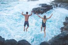 Couple jumping off cliff into turbulent ocean