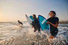 three people running into the surf with their boards