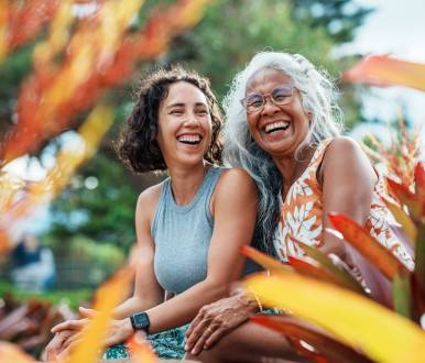 a hawaiian mother and daughter smile and sit in a garden