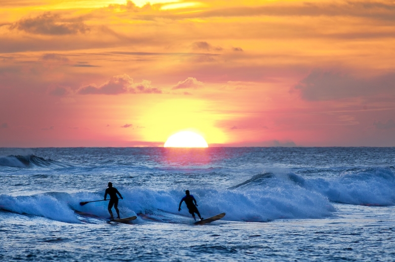 two people surfing and paddleboarding off Poipu Beach in Kauai