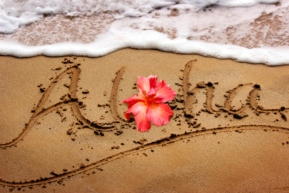 Aloha written in the sand with a flower where the letter o should be