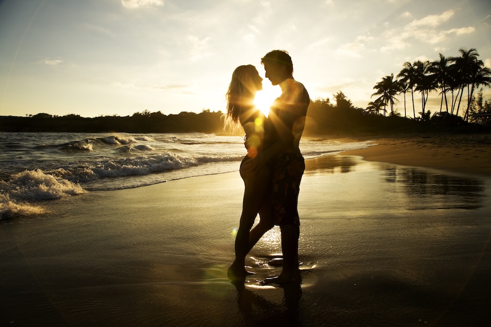 couple hugging on beach at sunset in hawaii