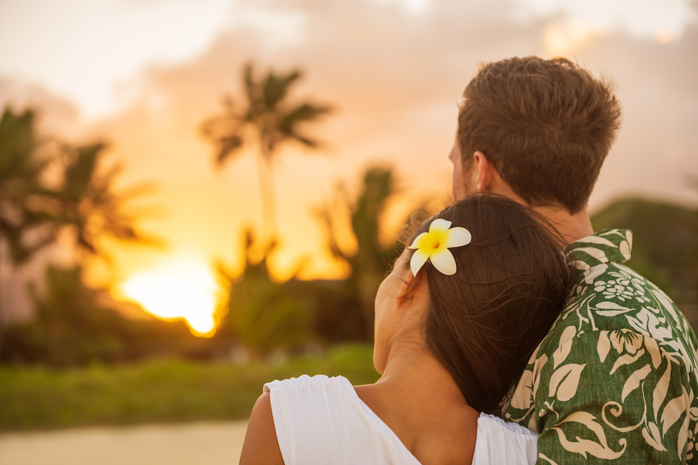 couple with backs turned to the camera watching sunset in hawaii