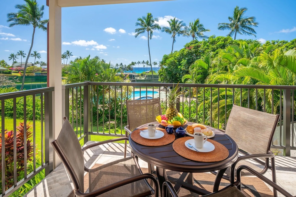 A table is set with plates, fruit, and coffee on the lanai at a Kauai vacation condo that overlooks the pool and ocean 