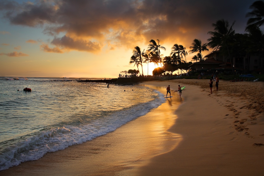 Sunset at Poipu Beach as surfers walk on the shoreline with their boards