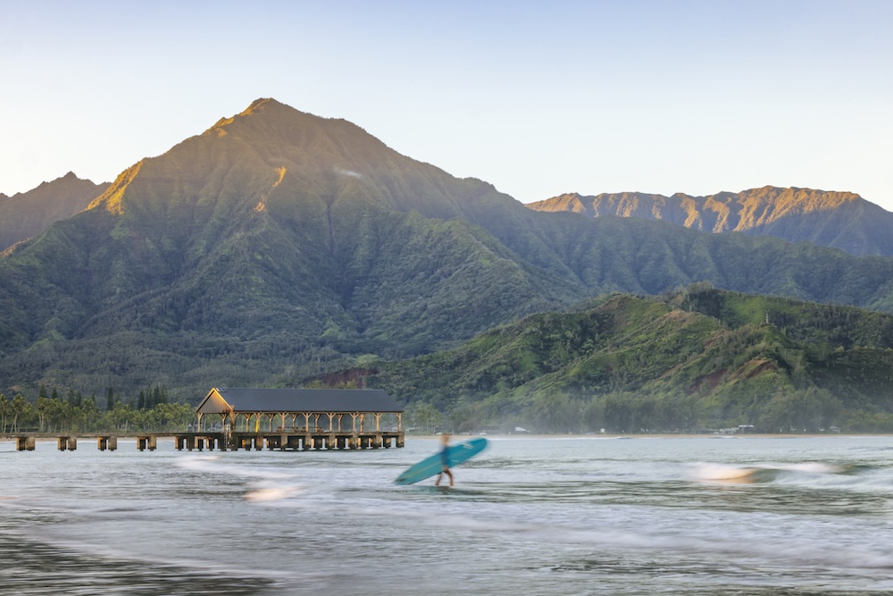 Person carrying a surfboard into the water at Hanalei Bay on Kauai